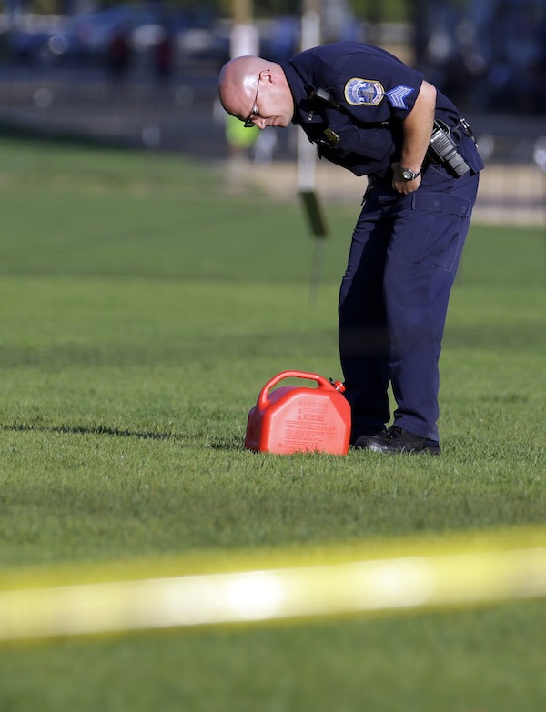 A police officer looks at a container at the scene on the National Mall in Washington, where, according to a fire official, a man set himself on fire Friday, Oct. 4, 2013. The official said the man was flown by helicopter to a hospital. (AP Photo/Alex Brandon)