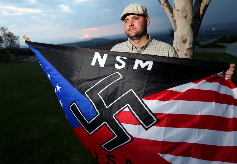 In this Oct. 22, 2010 file photo, Jeffrey Hall, who was killed by his then-10-year-old son, holds a neo-Nazi flag while standing at Sycamore Highlands Park near his home in Riverside, Calif. A California judge ruled Thursday, Oct. 31, 2013, that the boy, now 13, will spend at least the next seven years in a state juvenile facility. Judge Jean R. Leonard said the maximum the boy can serve would be until he is 23. He'll be eligible for parole in seven years. The decision came after prosecutors and defense attorneys argued for months about the best placement to assure his safety and rehabilitation.