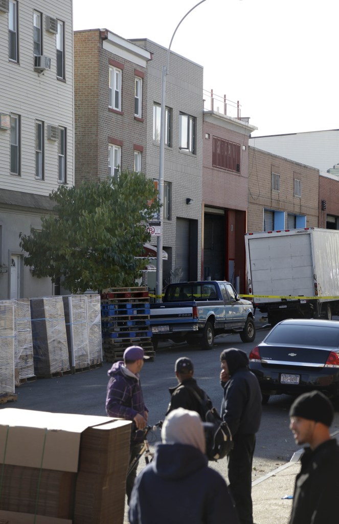 People stand near a row house, center, that was the location of a murder-suicide in the Brooklyn section of New York on Monday. A musician shot and killed two members of an Iranian indie rock band and a third musician early Monday, and wounded a fourth person at their apartment before killing himself on the roof, police and the group’s manager said.