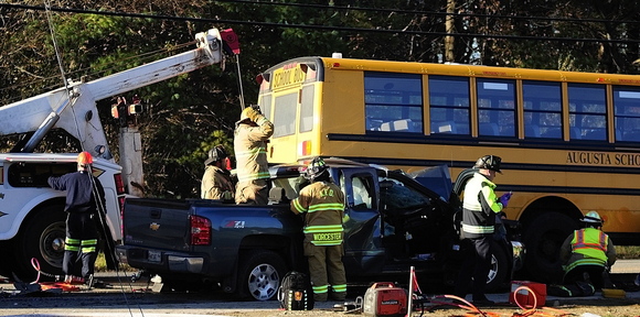 A tow truck lifts a school bus off a pickup truck as emergency crews work to free the pickup truck driver at the scene of a crash involving a school bus Tuesday on Riverside Drive in Augusta.
