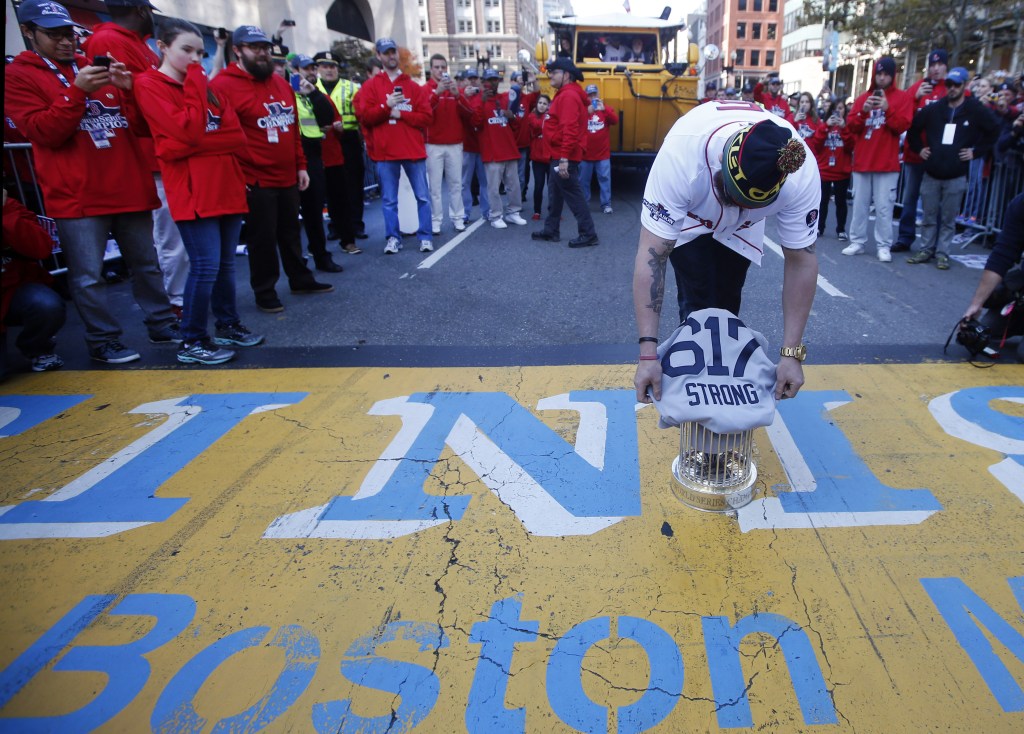 Boston Red Sox’s Jonny Gomes places the championship trophy and a Red Sox baseball jersey at the Boston Marathon finish line during a pause in their World Series victory rolling rally in Boston on Saturday to remember those affected by the Marathon bombing.