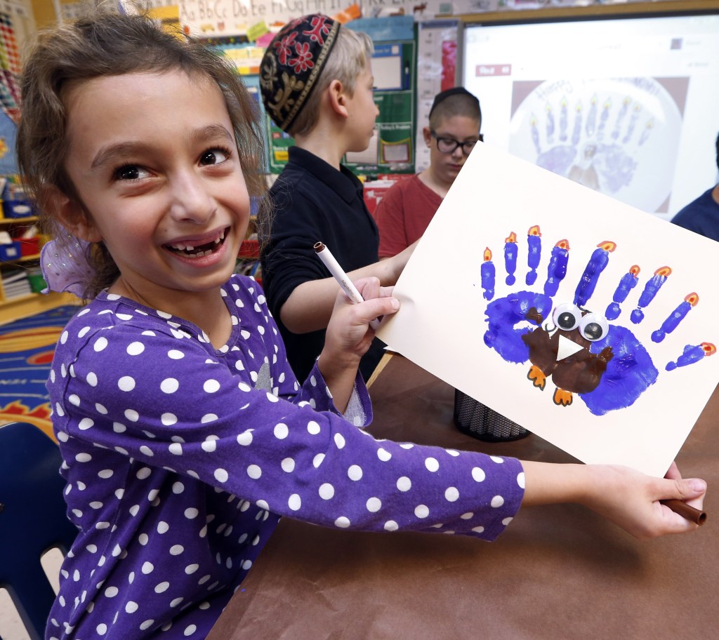 Rozie Aronov, 7, holds up a “menurkey,” a paper-and-paint mashup of a menorah and a turkey that she made at Hillel Day School in Farmington Hills, Mich., last week. A rare quirk of the calendar this year overlaps Thanksgiving with the start of Hanukkah. In many ways, a reader says, the two holidays are celebrated similarly.