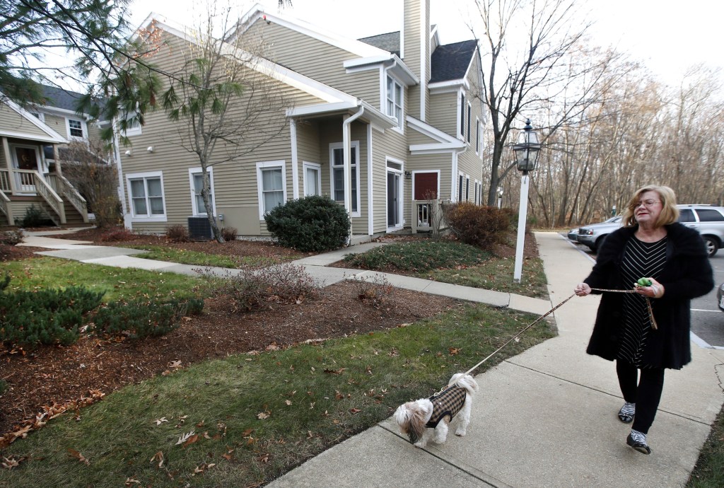Barbara Kansky, condo manager of Devon Wood in Braintree, Mass., walks her dog, Justine, along a sidewalk on the 350-acre property. Kansky turned to DNA testing to identity lawn-fouling dogs, yielding immediate and dramatic results.