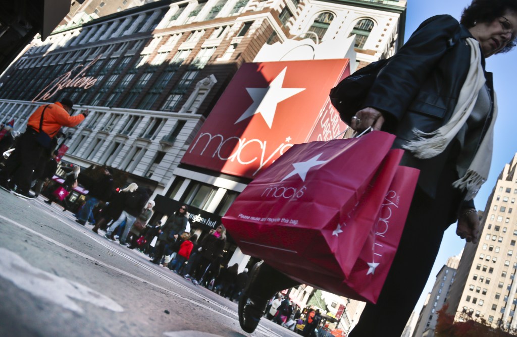 A shopper carries Macy’s bags while crossing an intersection outside Macy’s on Saturday, Nov. 23, 2013, in New York.
