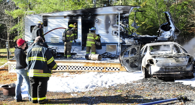Laura Ellis, left, speaks with a firefighter as others extinguish the destroyed remains of a camper she was staying in Tuesday on Beach Road in South China. Ellis was staying at friend and owner Tim Elkin’s camper when she started her car, right, which caught fire, then ignited the camper.