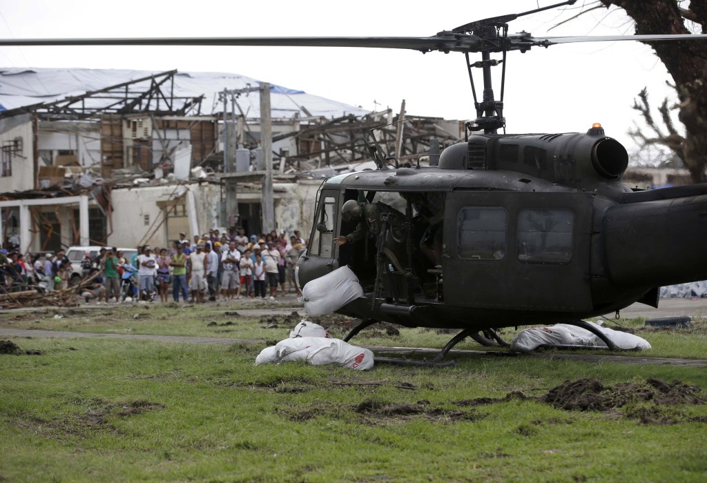 Typhoon survivors watch as a Philippine Air Force helicopter unloads sacks of relief supplies at Tanauan township, Leyte province in central Philippines on Friday, two weeks after Typhoon Haiyan ravaged central Philippines.