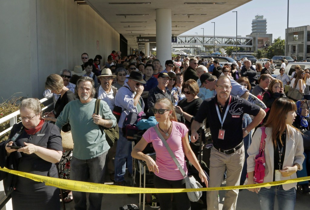 Passengers evacuated from Terminal 1 wait outside Los Angeles International Airport on Friday after shots were fired, prompting authorities to evacuate a terminal and stop flights headed for the city from taking off from other airports.