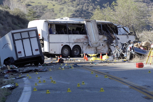 In this Feb. 4, 2013, photo, evidence markers dot the road in front of the wreckage of a tour bus that crashed in the Southern California mountains near San Bernardino. Seven passengers and a pickup truck driver were killed, 11 passengers were seriously injured and 22 others received minor to moderate injuries. The bus driver told passengers the vehicle’s brakes had failed.