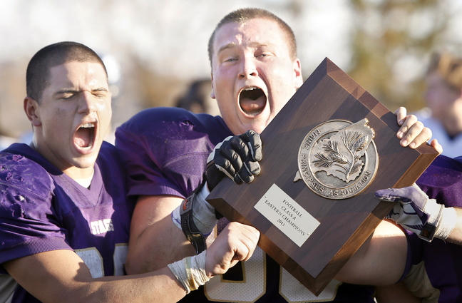 Cody O’Brien, left, and Greg Grinnell – the Cheverus High captains – celebrate with the Eastern Class A championship trophy Saturday after the Stags rallied to a 22-19 victory at home against Portland, earning a berth in the state final against Bonny Eagle.
