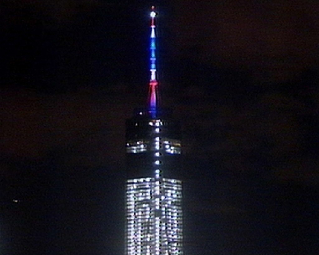 In this image taken from video, colored lights illuminate One World Trade Center as the building conducts its first beacon test last Friday in New York.