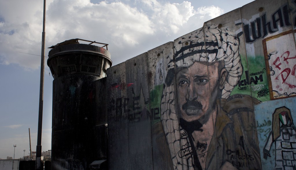A man walks past a section of the separation barrier with graffiti depicting the late Palestinian leader Yasser Arafat in the West Bank city of Ramallah on Friday, nearly nine years after Arafat’s death.