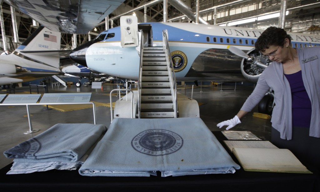 Lonna McKinley of the National Museum of the U.S. Air Force, looks through the log for President John F. Kennedy’s Air Force One, seen behind her, on Friday at the museum in Dayton, Ohio. The blanket at center was used by President Kennedy on the plane, and the blanket at left was used by First Lady Jacqueline Kennedy on the plane.