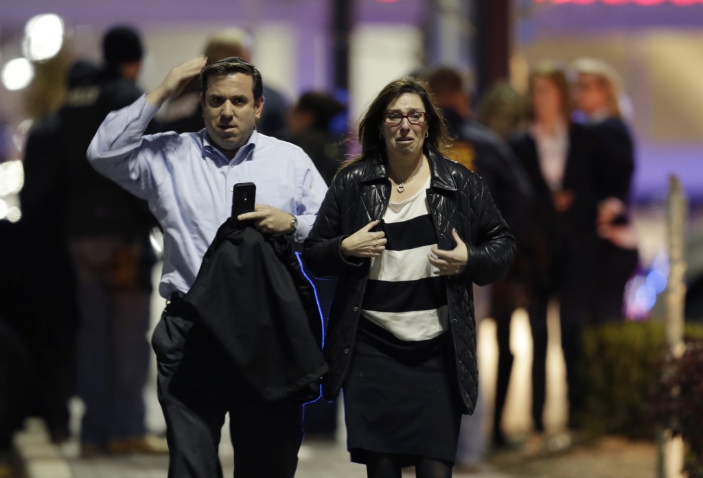 A man and woman leave the Garden State Plaza Mall with officials standing guard behind them Monday night.