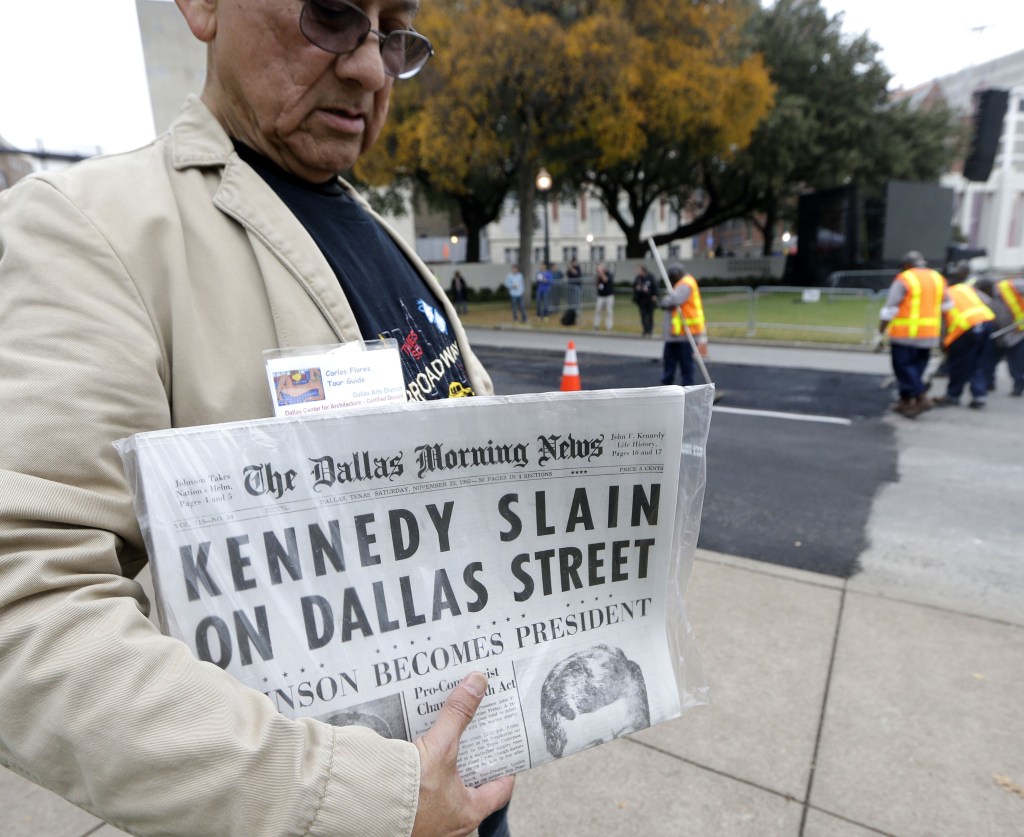 Carlos Flores holds a copy of the Dallas Morning News as crews finish up street work on Dealey Plaza in Dallas on Thursday. Dallas has planned a solemn ceremony Friday in the plaza President John F. Kennedy was passing through when shots rang out.