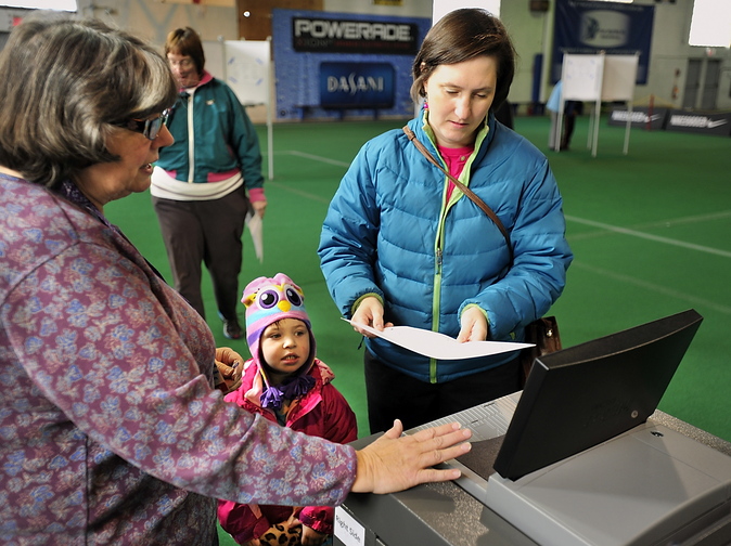 Erin Segal, 3, watches as an election clerk helps Erin’s mother, Amy Segal, process her ballot at one of 500 new voting machines provided by the state to precincts with more than 1,000 voters. She was voting at the National Guard Armory on Stevens Avenue in Portland.