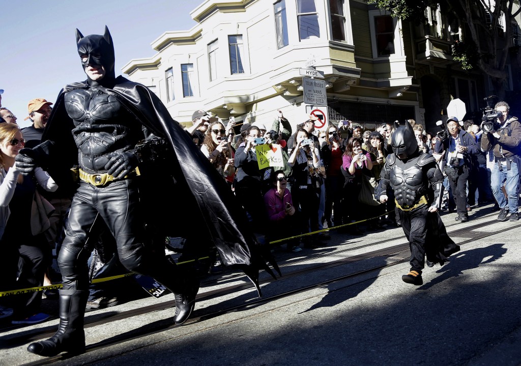 Miles Scott, dressed as Batkid, runs with Batman after saving a damsel in distress.