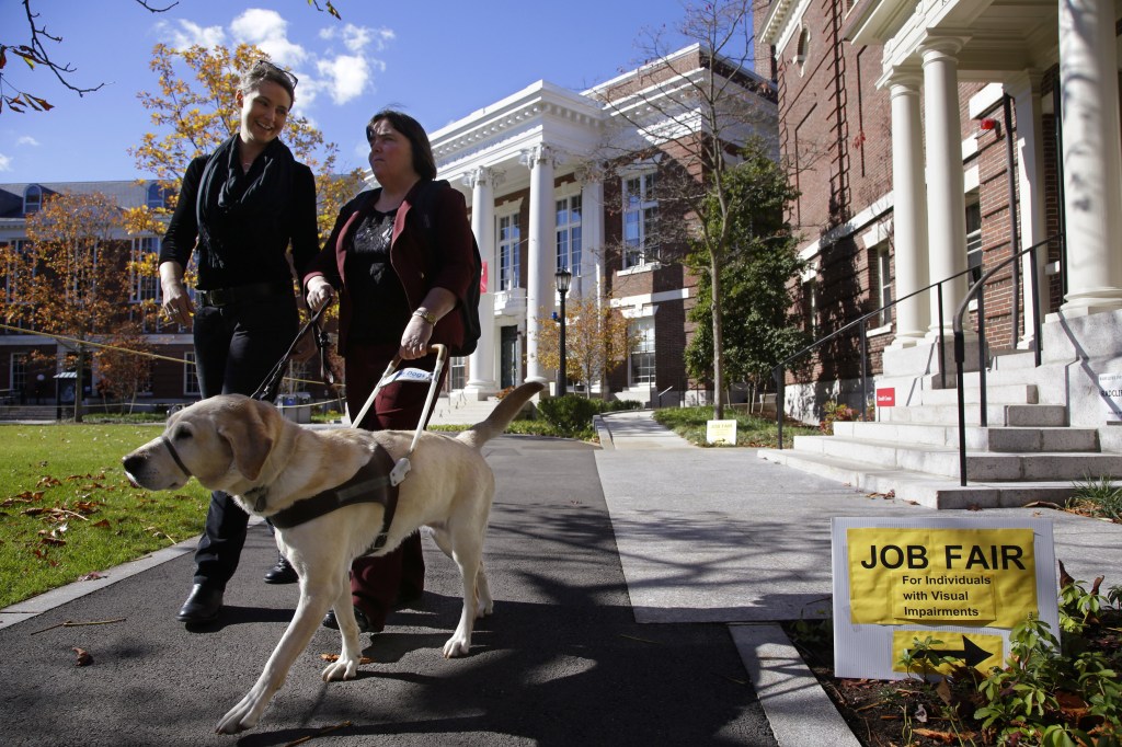 Marie Hennessy, president of the Perkins School for the Blind alumni association, leaves a job fair for the visually impaired accompanied by her guide dog, Azalea,, and a volunteer guide, left, on the Radcliffe Yard campus in Cambridge, Mass. Despite technological advances that dramatically boost their capabilities, blind people remain largely unwanted in U.S. workplaces. About 24 percent of working-age Americans with visual disabilities hold full-time jobs.