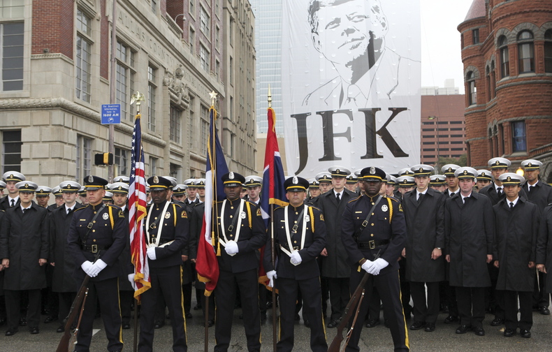 The Dallas Police Honorary Color Guard and the U.S. Naval Academy Men’s Glee Club pose in front of a giant JFK banner at ceremonies commemorating the 50th anniversary of the death of President John F. Kennedy in Dealey Plaza in Dallas on Friday. Left: President Kennedy and first lady Jackie Kennedy.