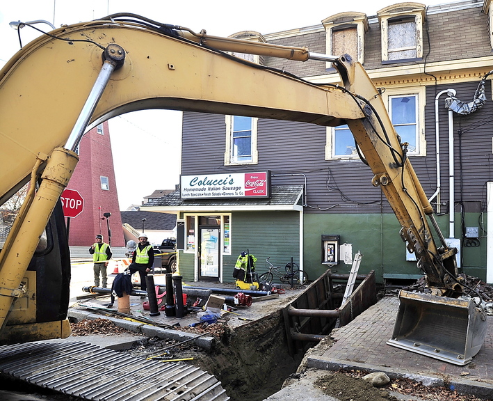 Framed by a large excavator, workers wait for a plumber to install the feed from the water main for sprinklers that will be installed throughout Colucci’s Hilltop Superette at 135 Congress St. The building, damaged by an arson fire in March, has Colucci’s on the ground floor and three upper-floor apartments.