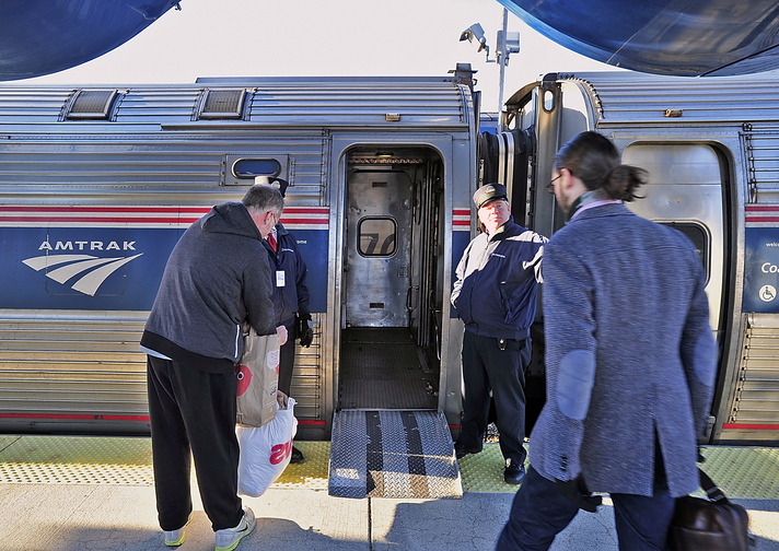 Conductors Brad Ritter, left, and Brian Labreck assist passengers as they board the Downeaster in Portland for a trip south to Boston.