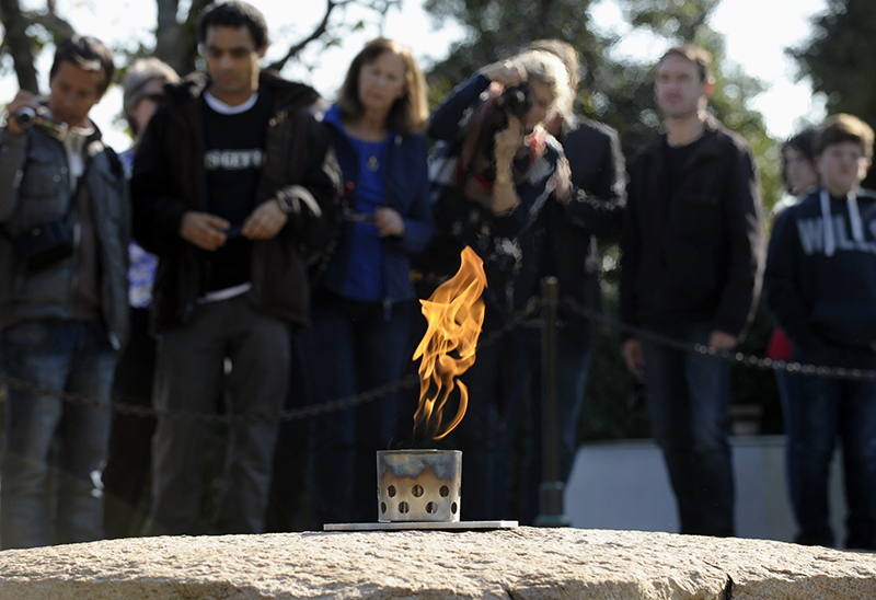 In this Tuesday, Oct. 29, 2013 file photo, visitors stand near the eternal flame at the grave site of U.S. President John F. Kennedy at the Arlington National Cemetery in Arlington, Va. The cemetery transferred the flame from a temporary burner to the restored permanent eternal flame that is part of a memorial to the 35th president. Repairs began in April 2013 to replace components of the eternal flame's burner.