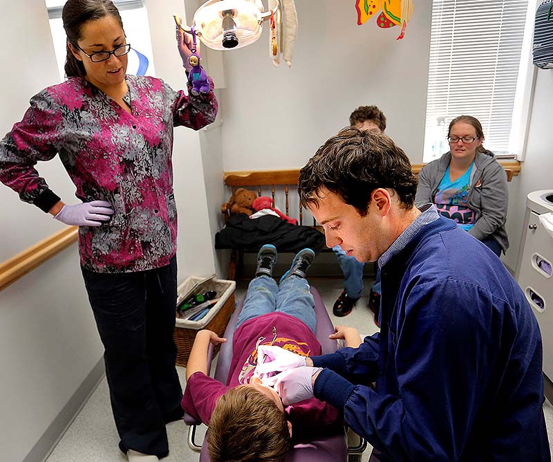 Dr. Michael Dowling, right, works on patient Aiden Serber, 8, of Westbrook, as dental hygenist Trisha Drewry, left, assists at Falmouth Pediatric Dentistry in Falmouth on Wednesday. The practice treats about 10,000 MineCre patients, said Dowling, a co-owner.