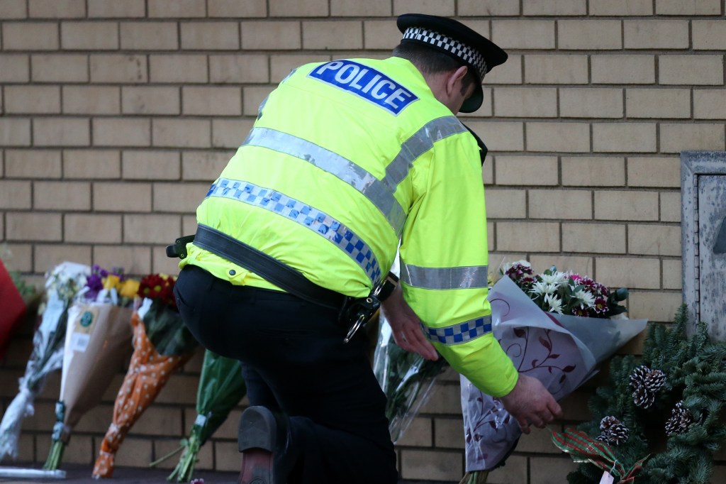 An officer arranges flowers Saturday after a helicopter crash at The Clutha pub in Glasgow, Scotland. A rescue and recovery operation is ongoing and could bring more bad news.