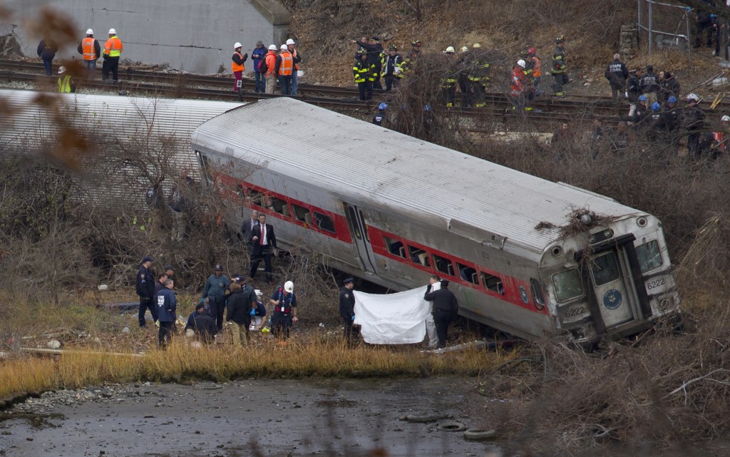 Viewed from Manhattan, first responders and others work at the scene of a derailed Metro-North passenger train in the Bronx borough of New York on Sunday. The train derailed on a curved section of track in the Bronx, coming to rest just inches from the water, killing at least four people and injuring more than 60, authorities said. Police divers searched the waters to make sure no passenger had been thrown in, as other emergency crews scoured the surrounding woods.