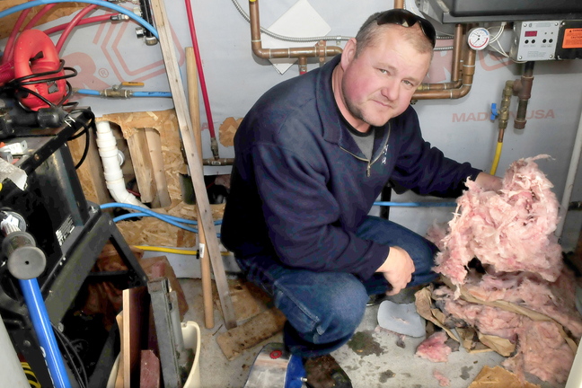 DAMAGE: Inside a furnace room in Jean Mosher’s home in Smithfield, her son Andy Landry holds insulation that he said rats from a neighbor’s pig farm pulled from a wall. At left are holes in the walls that were made to gain access to repair pipes damaged by the rats.