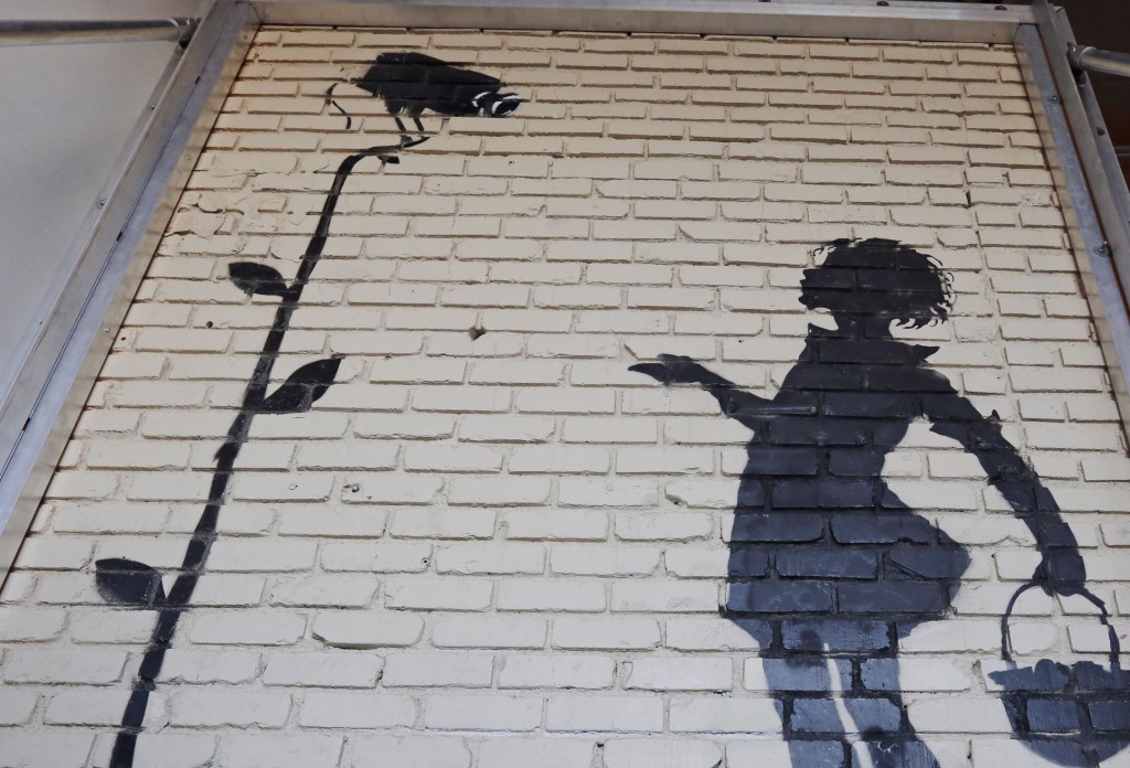 “Flower Girl,” a delicate stencil on a massive brick wall by popular street artist Banksy, is shown on display.
