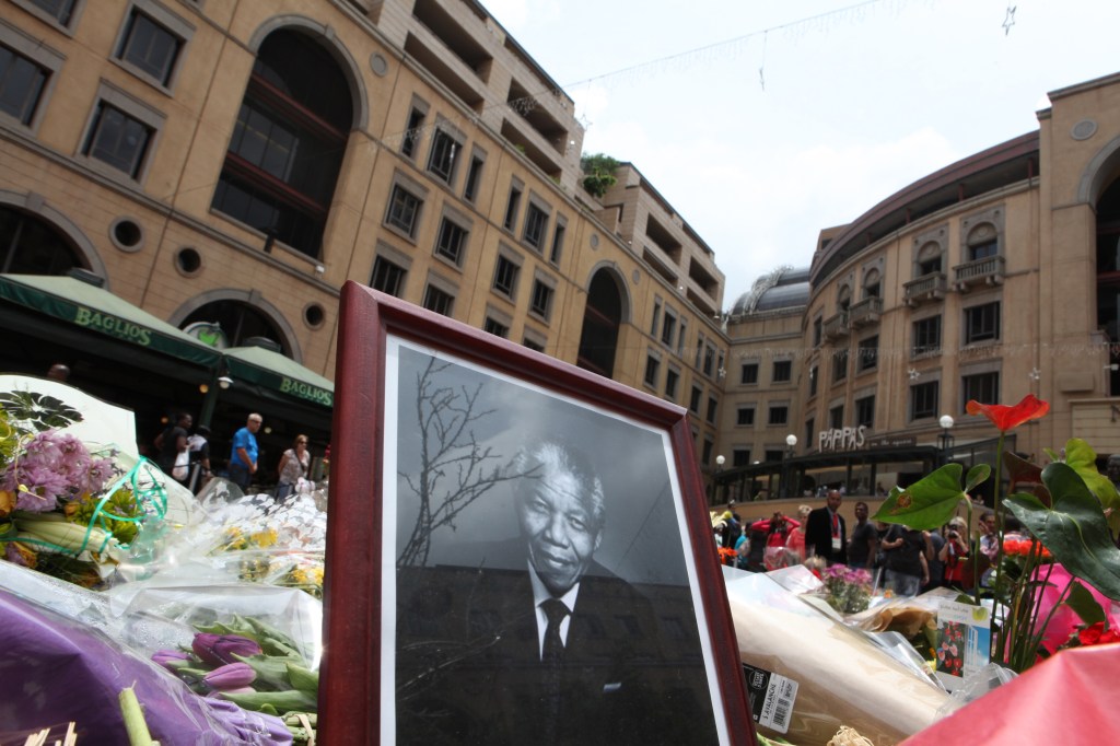 A portrait of former South African President Nelson Mandela is placed among a pile of flower tributes in Sandton, Johannesburg, South Africa, Saturday, Dec. 7, 2013. Mandela died Thursday at his Johannesburg home after a long illness. He was 95.