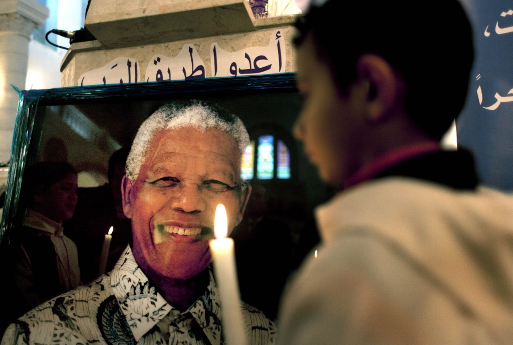 A Palestinian child holds a lit candle as he prays in front of a poster of late South African leader Nelson Mandela, during a special service in his honor at the Holy Family Church, in the West Bank city of Ramallah, on Sunday.