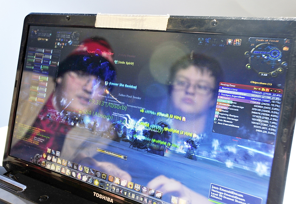 Victor Smith of Portland, right in reflection, plays his customized character with dozens of others online Thursday in “World of Warcraft.” Helping Smith with strategy at R Choice 2 Gaming in Portland is his friend, Keegan Beal.