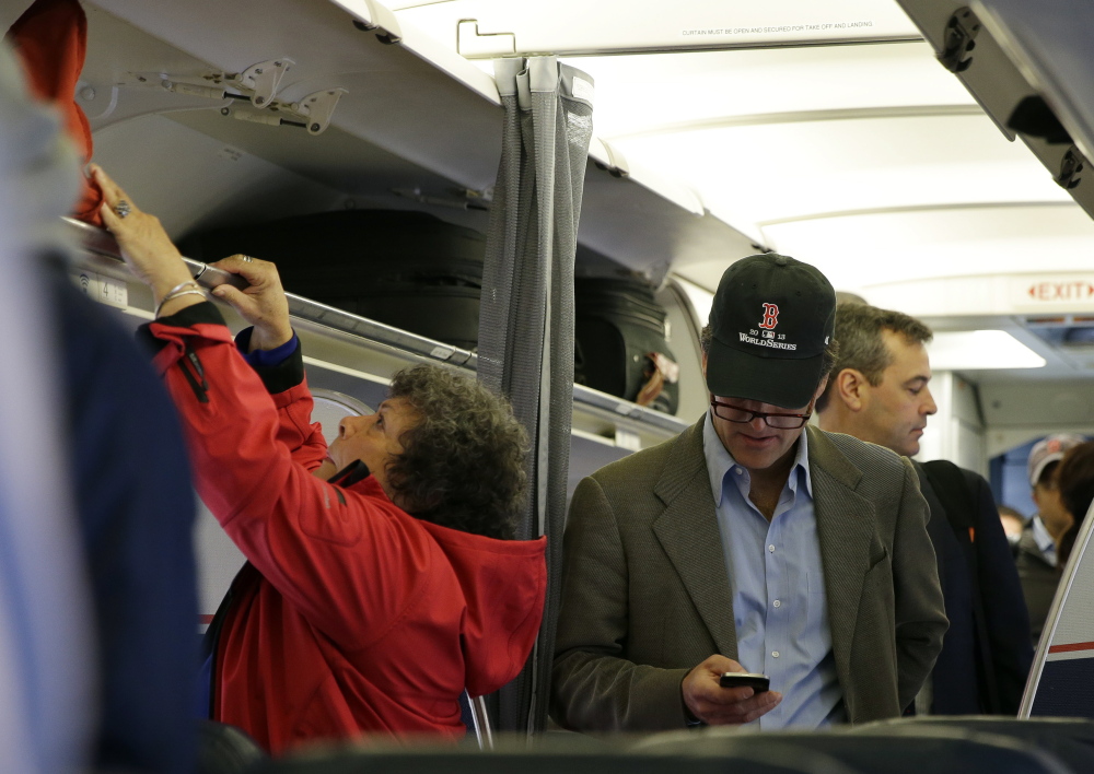 A passenger checks his cellphone while boarding a flight in Boston. For the past decade, fliers haven’t been able to use electronic devices while planes are below 10,000 feet because they might interfere with cockpit instruments, but the Federal Aviation Administration has decided that interference isn’t a concern anymore.