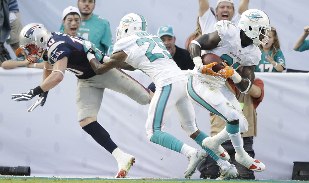 Miami’s Michael Thomas intercepts a Tom Brady pass intended for New England receiver Austin Collie, who’s double-teamed by Will Davis, on the last play of Sunday’s game in Miami Gardens. Despite the loss, the Patriots still are in control of the AFC East and could wrap up the title with a win in the next two weeks.
