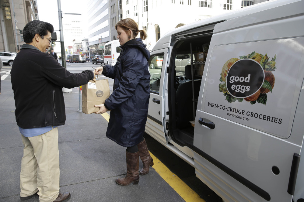 Good Eggs community dispatcher Vanessa Casey, right, hands an order to a Financial District customer in San Francisco. New online services are letting consumers buy fruits, vegetables, meats and artisan foods directly from local farmers and producers. Buyers can have their orders delivered or retrieve them at local pickup spots.