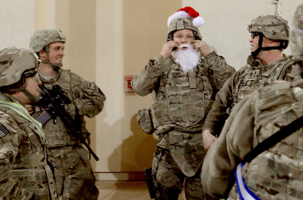 Sgt. Alan Feener of Jefferson adjusts his Santa hat and beard to fit over his body armor as a group of carolers from the 133rd Engineer Battalion of the Maine Army National Guard stopped by some of the barracks at Bagram Air Field in Afghanistan to sing Christmas songs before a church service Tuesday, December 24, 2013.