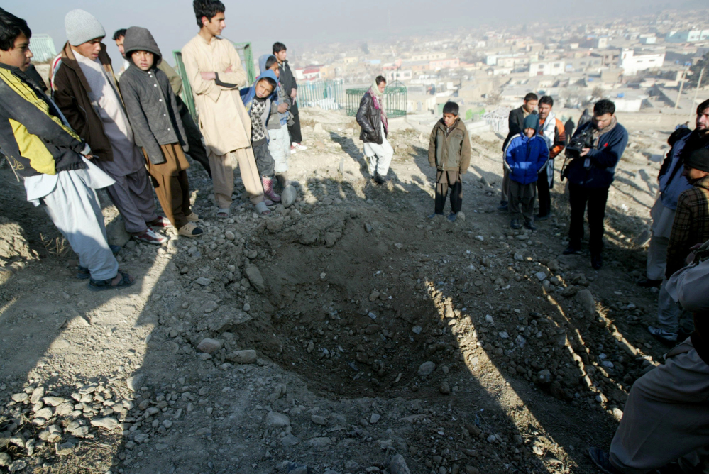 Afghan people stand near a crater from an attack targeting the U.S. embassy in Kabul, Afghanistan, Wednesday, Dec. 25, 2013. The U.S. Embassy in Afghanistan says its compound was hit by indirect fire just before dawn on Christmas Day. It says no Americans were injured.