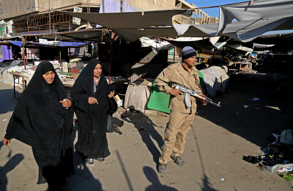 An awakening council member stands guard while women walk through the site of a bombing in a Christian section of Baghdad, Iraq, Wednesday, Dec. 25, 2013. Militants in Iraq targeted Christians in two separate bomb attacks in Baghdad, officials said. The Christmas Day attacks brought the total number of people killed so far this month in Iraq to 441. According to U.N. estimates, more than 8,000 people have been killed since the start of the year.