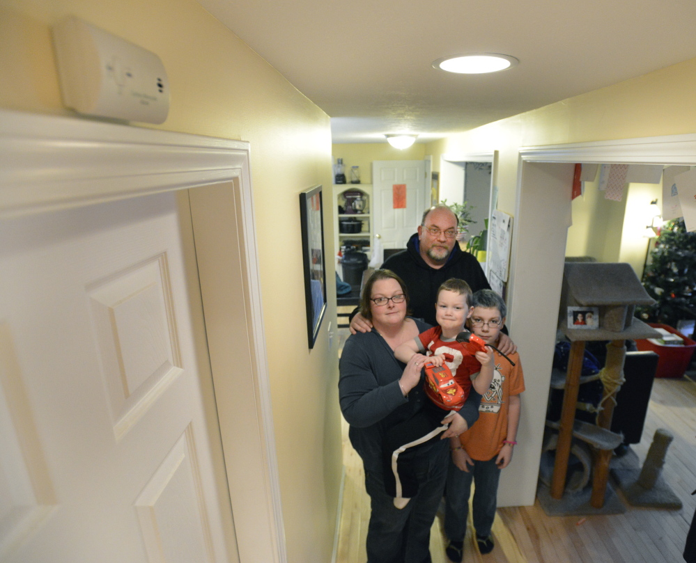 Heather and Bob Mills and their children, Cooper, 4, and Trenton, 11, stand in the hallway of their Biddeford home, where they installed another carbon monoxide detector, upper left, after the four were poisoned by the deadly gas in February.