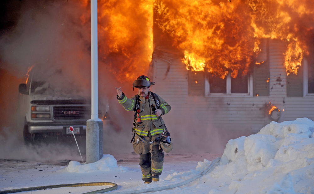 A Waterville firefighter gestures to other first responders on Christmas Day as they arrive to battle a fire that destroyed a garage used for storing flooring supplies.