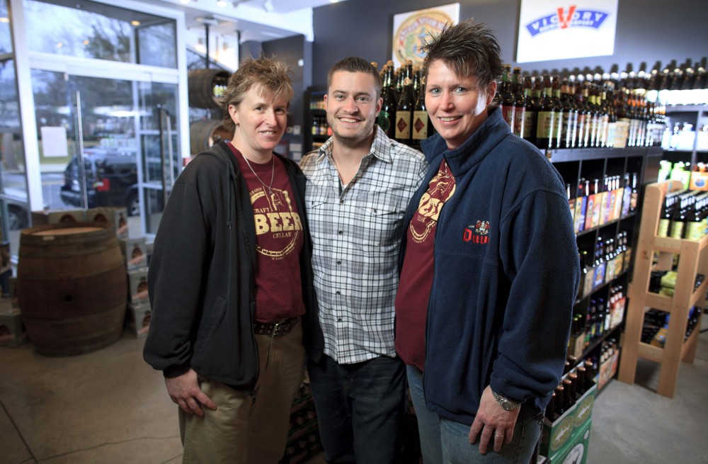 Craft Beer Cellar founders Kate Baker, left, and Suzanne Schalow, right, pose with Craft Beer Cellar store owner Brian Shaw in Newton, Mass. Beers there are organized by region, from Worcester to the West Coast, with an emphasis on local brews.