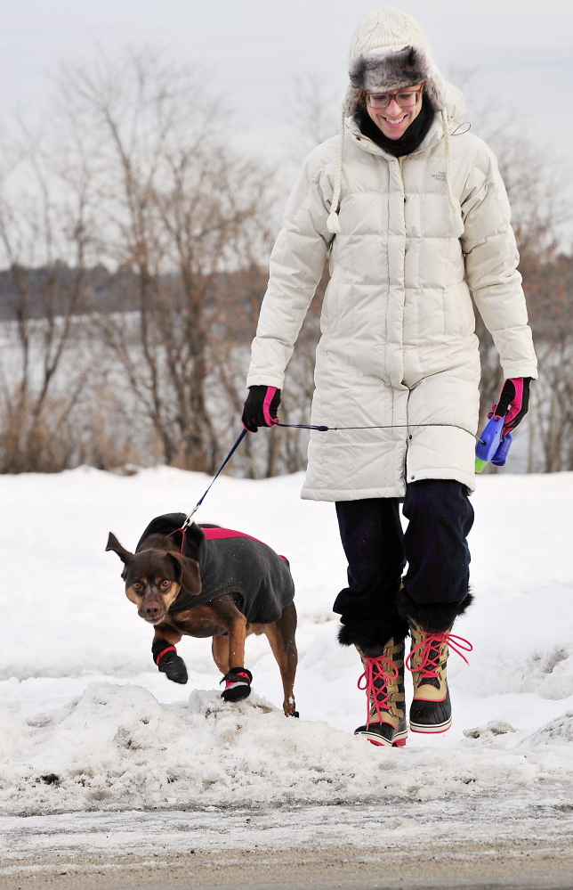 Dressed for the cold weather, Margaret Ybarra walks her dog Hunter, who is dressed in warm boots, along the Eastern Prom in Portland on Tuesday.