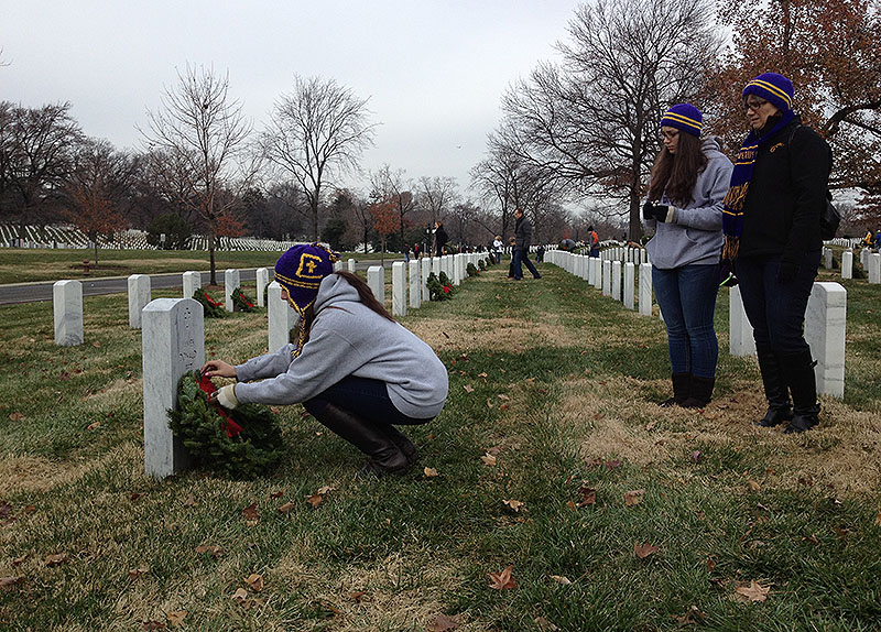 Alexia Fornaro of Portland lays a wreath against a grave at Arlington National Cemetery in Virginia on Saturday as her sister and mother, Daniela and Giulia, look on. The family traveled to Arlington as part of a group from Cheverus High School participating in the Wreaths Across America ceremonies on Saturday.