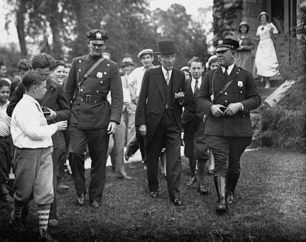 In this May 14, 1933 photo, John D. Rockefeller Sr. is surrounded by state troopers and admirers as he attends church in Lakewood, N.J. “Names like Carnegie, Mellon and Rockefeller – the Buffet and Gates of their days – grace universities, museums and medical centers in part because the originators of those fortunes gave back,” Harvard Business School professor Michael Norton says.