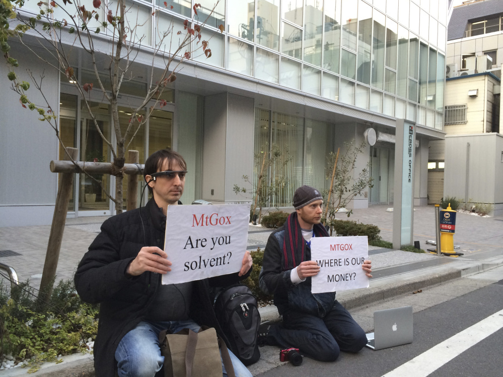 Bitcoin trader Kolin Burges, right, of London, and an American who would only give his first name, Aaron, hold protest signs as they conduct a sit-in in front of the office tower housing Mt. Gox in Tokyo on Tuesday. The website of major bitcoin exchange Mt. Gox went offline suddenly Tuesday. Burgess said he hopes to recoup $320,000 he has tied up with Mt. Gox.