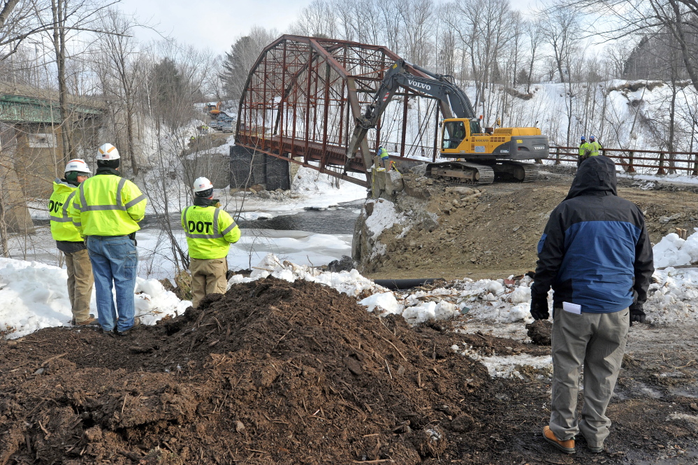 An excavator digs the embankment away from the New Sharon bridge next to Route 2 during demolition Thursday.