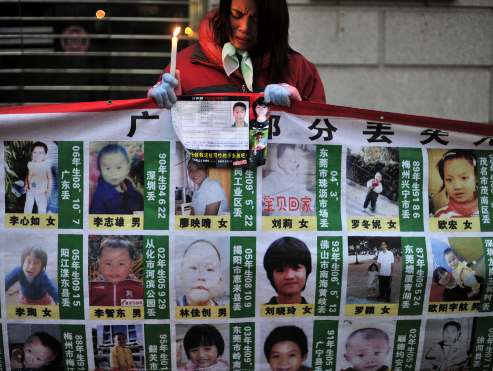 A woman holds a candle behind a board showing photos of missing children during a campaign to search for them in Wuhan, in central China’s Hubei province.