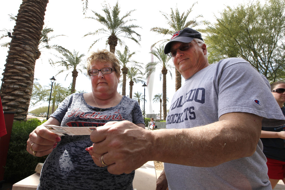 In this photo taken Wednesday, Feb. 26, 2014, Sue Knieriemen, of Fremont, Ohio, and her brother Charles Bork, of Sylvania, Ohio, check their tickets outside Goodyear Ballpark before an exhibition baseball game between the Cincinnati Reds and the Cleveland Indians in Goodyear, Ariz. After such a long, cold season, Americans across the winter-weary Midwest and the East Coast are desperate to escape to warm-weather destinations in California, Arizona and Florida.