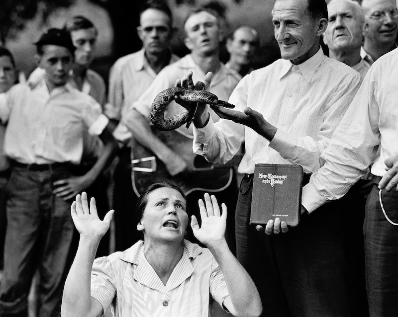 In this Aug. 22, 1944 file photo, members of the Pentecostal Church of God, a faith healing sect, surround a woman who has "Got the Spirit" as a man holds a snake above her head in Evarts, Ky. Although a Kentucky statute passed in 1940 prohibits the handling of snakes in connection with religious services, this sect revived the ritual after the recent death of a native of the region who was bitten by rattlesnake. 1940s 40s Animal Back Woods Bible Book Charmer Christians Cult Danger Eerie Event Fear Guitar Handler Kneeling Men Odd Offbeat Religion Risk Rural Sect Serpent Snake Speaking in Tongues Spirituality Standing State Strange Trance Trust Watching Women